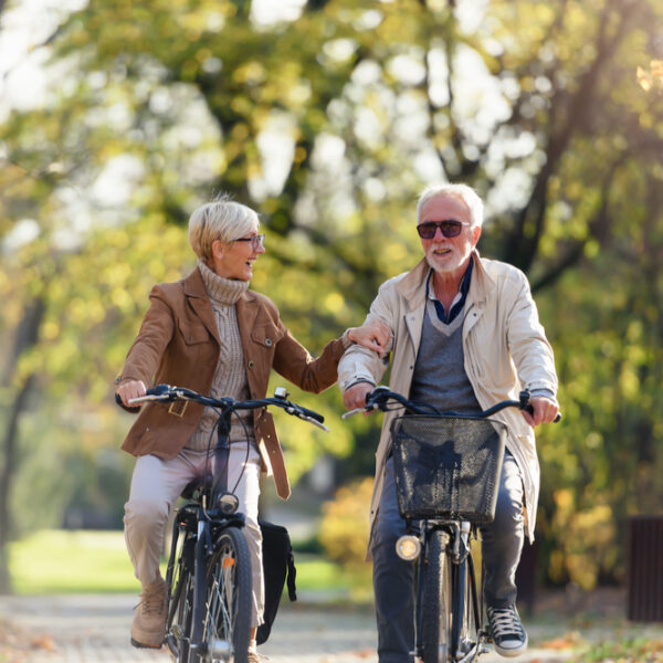 Cheerful active senior couple with bicycle in public park together having fun