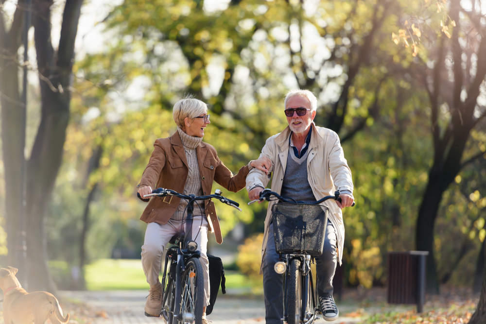 Cheerful active senior couple with bicycle in public park together having fun